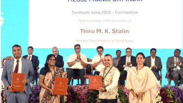 MoU ceremony with officials holding agreements, seated guests in the background, floral arrangements, bright blue backdrop.