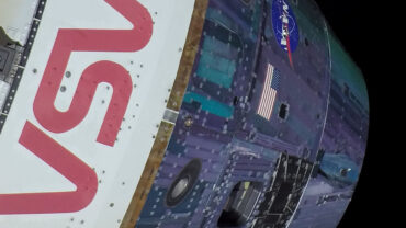 The image features a close-up of a spacecraft exterior with the bold "NASA" logo in red and a section with an American flag, set against a black background.