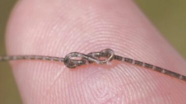 Close-up of a fine thread looped into a tight knot, resting on a fingertip with a soft, blurred background.