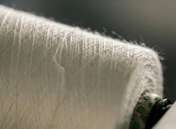 Close-up of a white spool of yarn with intricate texture, resting on a dark surface, highlighting its soft fibers and winding pattern.