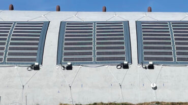 Curved concrete structure with four large solar panels mounted, set against a clear blue sky, highlighting renewable energy technology.