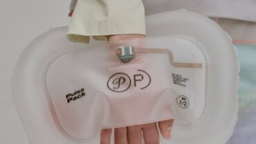 A person holds a transparent, soft Pulse Pack with a pink tint, featuring minimal branding, against a neutral background.