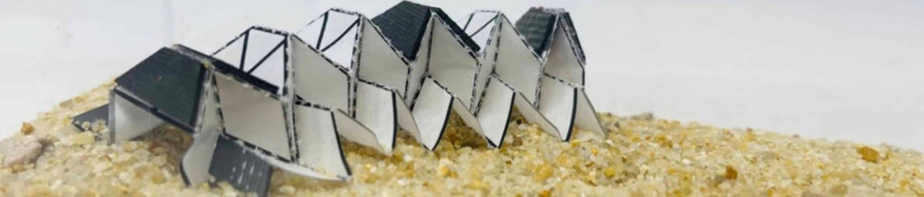 Abstract, folded structures with black tops and white bases arranged on a sandy surface, highlighting innovative biomedical textile design.