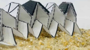 Abstract, folded structures with black tops and white bases arranged on a sandy surface, highlighting innovative biomedical textile design.