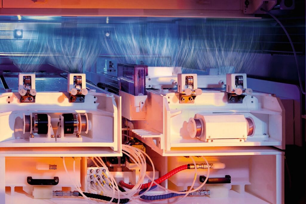 Close-up of a modern electrospinning machine, showcasing intricate white components, tubes, and visible fibers in a gradient light setting.