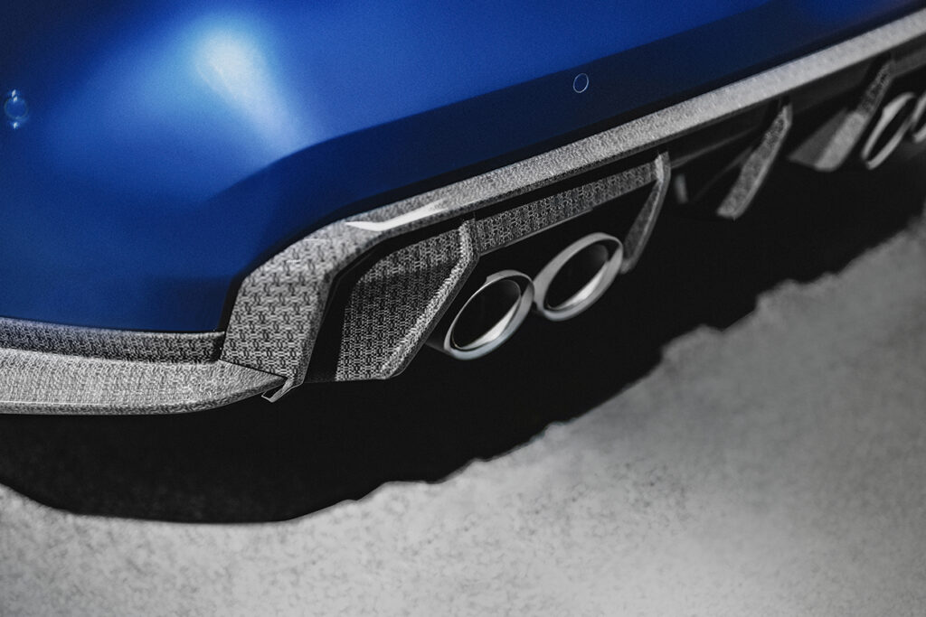 Close-up of a blue car's rear bumper featuring a textured gray fiber accent and dual chrome exhaust tips, set against a neutral background.
