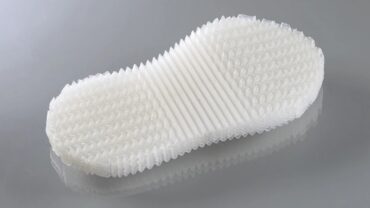 Textured, white shoe sole with a unique, ribbed design, placed on a reflective gray surface.