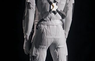 A grey, textured lunar suit with pronounced lines and straps, viewed from behind against a dark background.