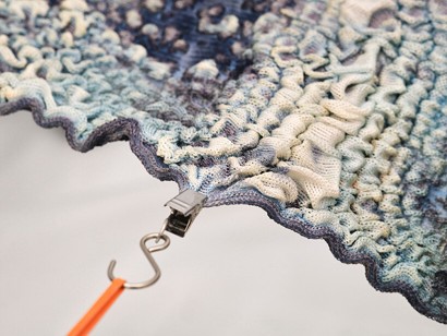Textured fabric in shades of blue and cream, featuring a wavy edge and a clip holding it in place, set against a neutral background.