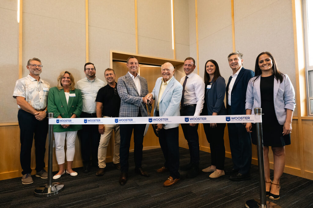 A group of professionals stands together, smiling, with a large ribbon and scissors at the center, signaling a grand opening event.