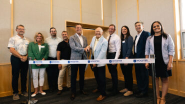 A group of professionals stands together, smiling, with a large ribbon and scissors at the center, signaling a grand opening event.