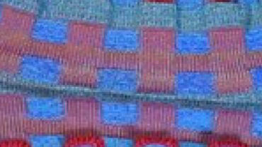 Close-up of hands holding a colorful, patterned textile with red, blue, and gray squares, highlighting the fabric's texture and design.