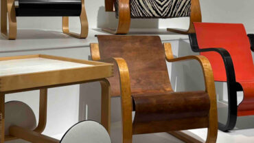 A display of modern chairs in various styles and colors, including red, black, and natural wood, arranged on a white platform.