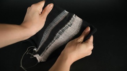 A person holds a flexible textile featuring alternating black and white stripes, showcasing its texture and adaptability against a dark background.