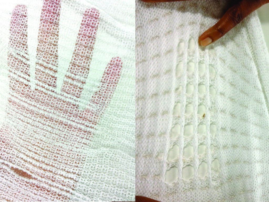 Close-up of a hand against a textured white knitted fabric, showcasing intricate patterns and openings in the material.