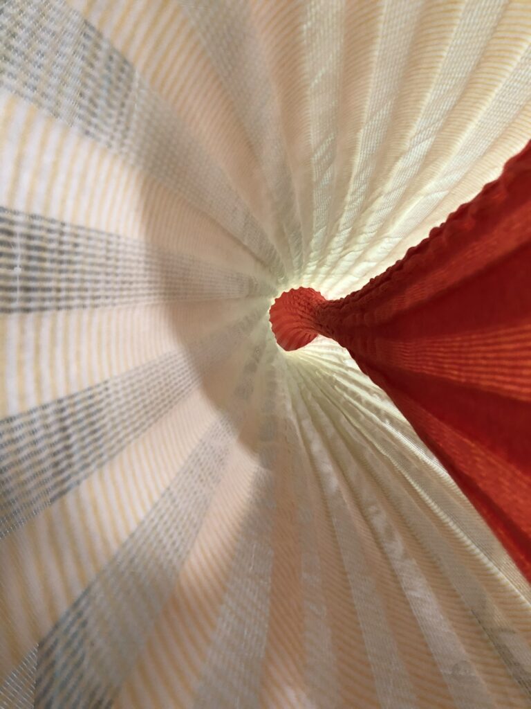 View from above a cone-shaped structure, featuring soft yellow and white stripes with a vibrant red peak at the center.
