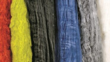 Strands of Nomex fiber displayed in assorted colors: red, yellow, black, blue, gray, and white, showcasing their textured surfaces.
