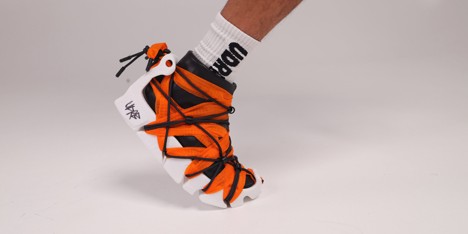 Sneaker featuring a black and white base with vibrant orange accents, uniquely laced with strings, showcased on a foot.
