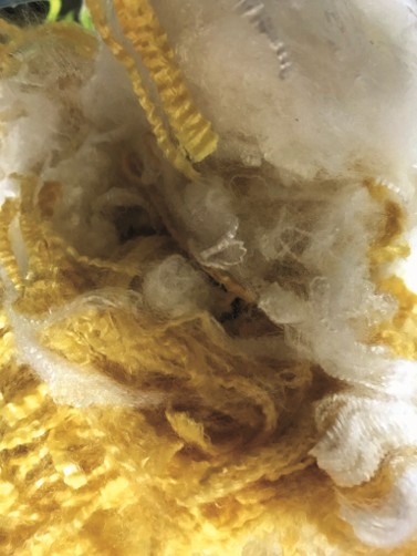 Close-up of pliable yellow and white staple fibers intertwined, showcasing a textured, soft surface with a mix of fibers.